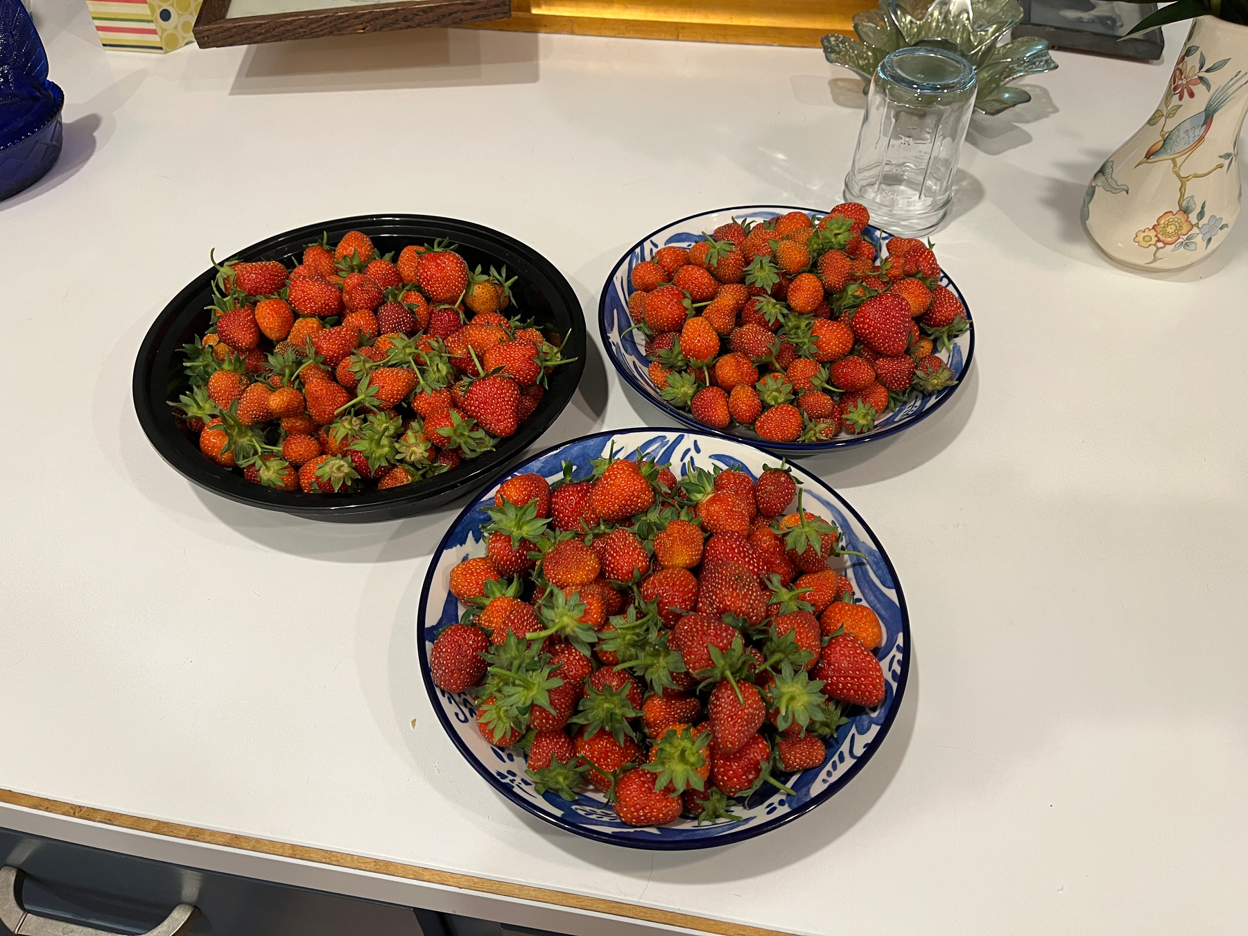 Three dishes filled with strawberries on a countertop.